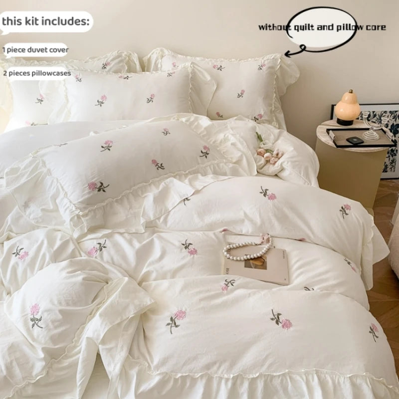 White duvet cover set with pink rose embroidery and lace details displayed on a bed.