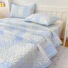 Light blue and white quilted bedspread with floral patterns and matching pillows on a bed.