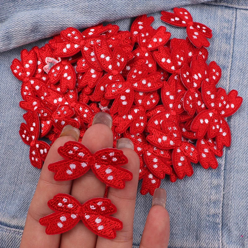 A hand holds a cluster of red embroidered cartoon bow iron-on patches on a denim fabric.