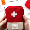 A red compact travel medicine organizer bag with a white cross emblem is held in a person's hand.
