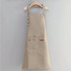 A beige canvas kitchen apron with chest pockets and a wooden hanger displayed against a light gray background.