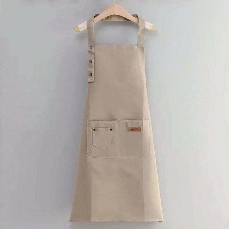 A beige canvas kitchen apron with chest pockets and a wooden hanger displayed against a light gray background.