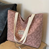 A pink corduroy tote bag with floral accents is displayed next to a black leather item.