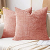 A square, textured terracotta pink cushion cover with a woven chenille finish resting on a light-colored fabric.