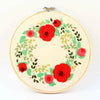 A round embroidery hoop featuring a red and green floral wreath design.