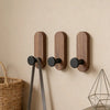 Three vertical walnut wood adhesive hooks mounted on a beige wall.