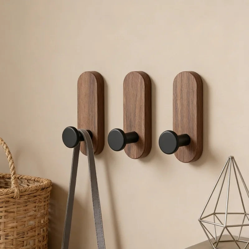 Three vertical walnut wood adhesive hooks mounted on a beige wall.