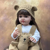 A baby doll wearing a knitted bear hat and overalls, with long dark hair.