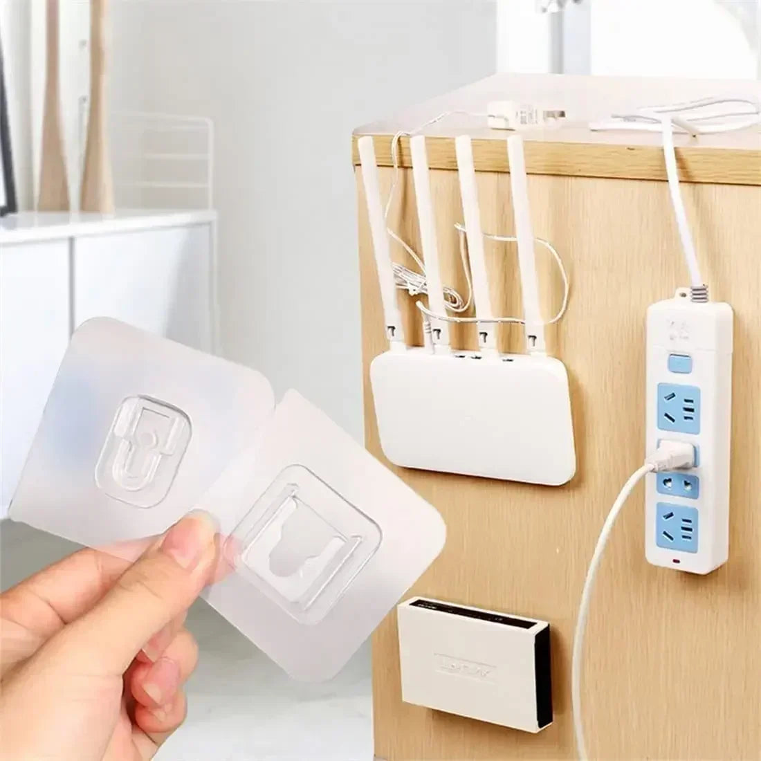 A hand is applying a clear double-sided adhesive wall hook to a wooden panel, next to the packaged hooks.