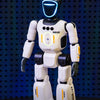 A white robot with a glowing blue head and orange accents stands on a dark surface.