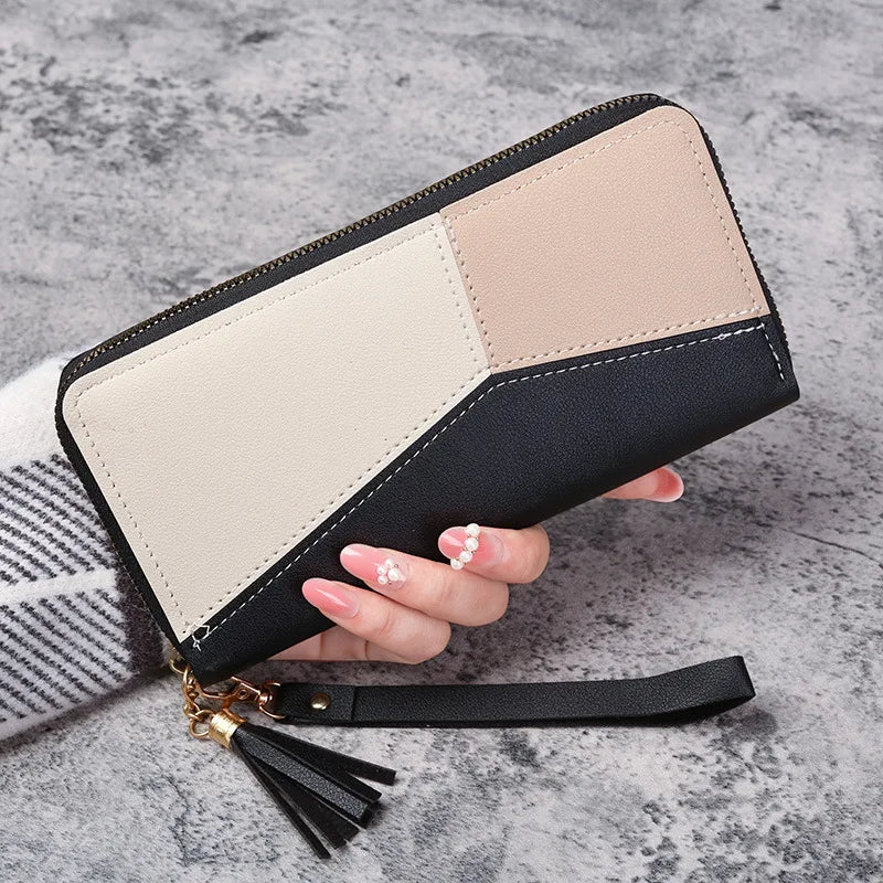 A beige and black quilted leather wallet with a gold tassel attached, shown being held by a hand.