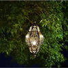 A decorative, ornate brass solar hollow-out lantern hanging from a tree branch in the dark.