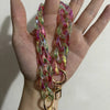 A close-up of a pink and green resin chain replacement strap with gold clasps held in a hand.
