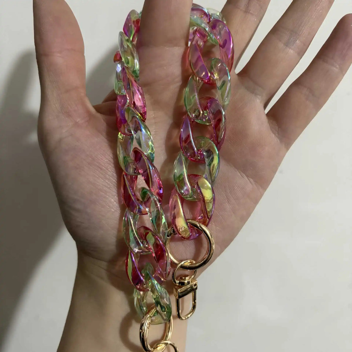 A close-up of a pink and green resin chain replacement strap with gold clasps held in a hand.