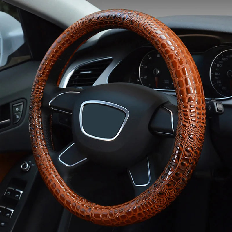 A close-up view of a brown crocodile grain leather car steering wheel cover installed on a black vehicle's steering wheel.