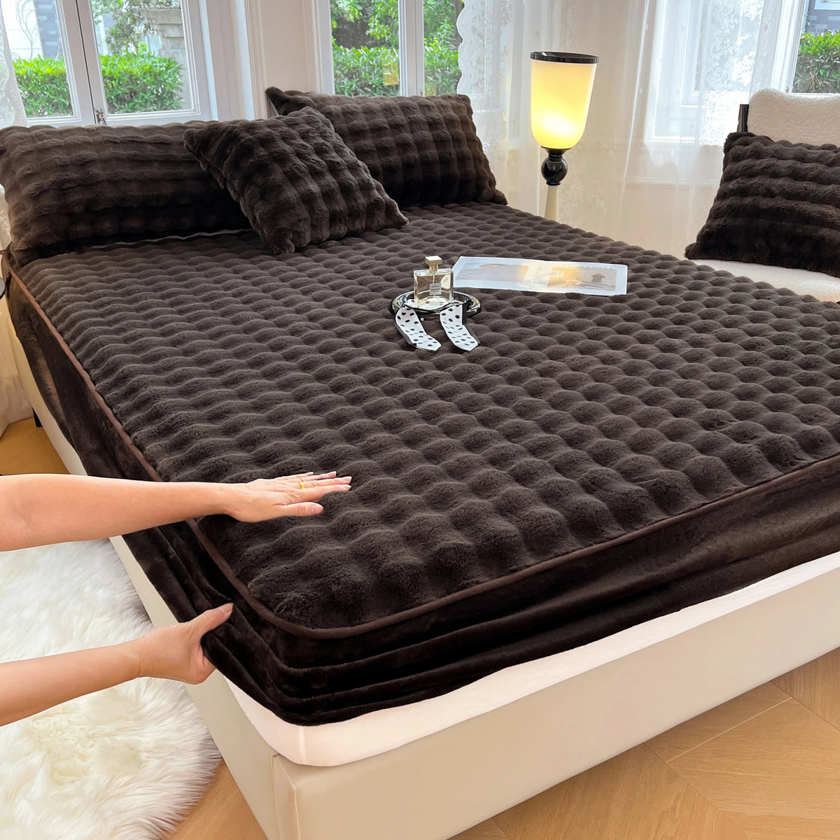 A dark brown luxury faux fur fitted sheet and pillowcase set is displayed on a bed with natural light.