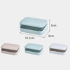 A set of three transparent soap dishes in pink, light blue, and white with drainage trays.