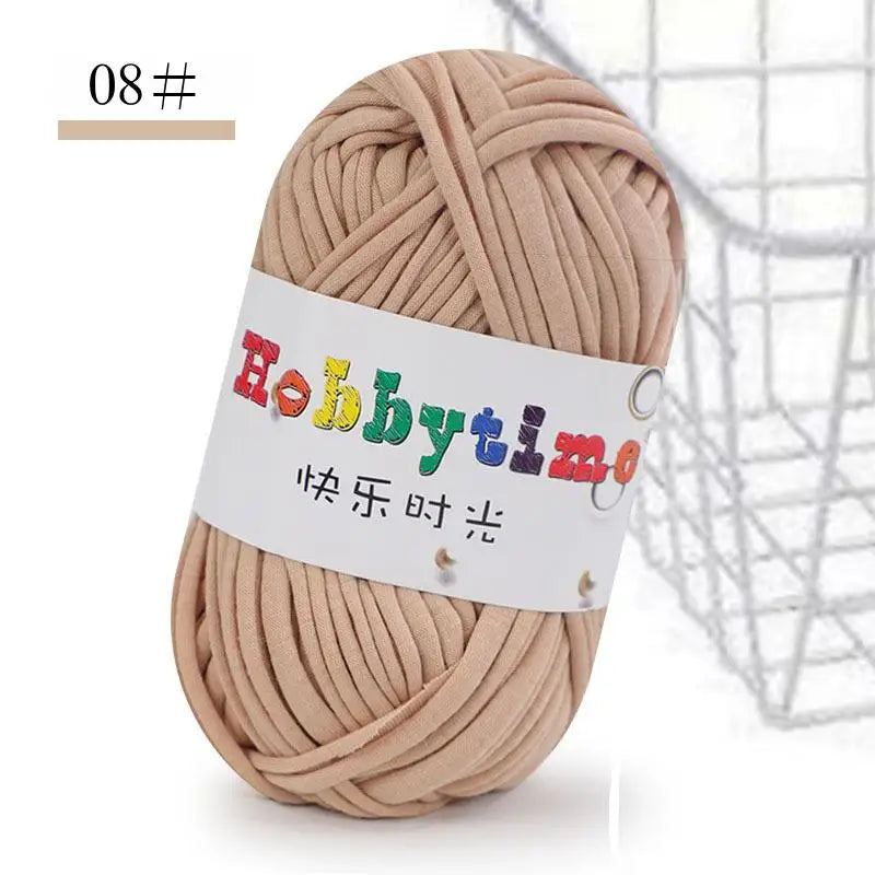 A ball of light beige soft T-shirt yarn for crochet and knitting is shown next to a wire mesh basket.