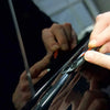 Hands are applying a glossy black vinyl wrap strip to a car trim piece.