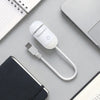 A white 2-in-1 mini projector night light with a flexible cord is shown on a gray surface next to a notebook and a laptop.