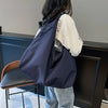 A person is standing next to a dark cabinet holding a navy blue lightweight nylon tote bag.
