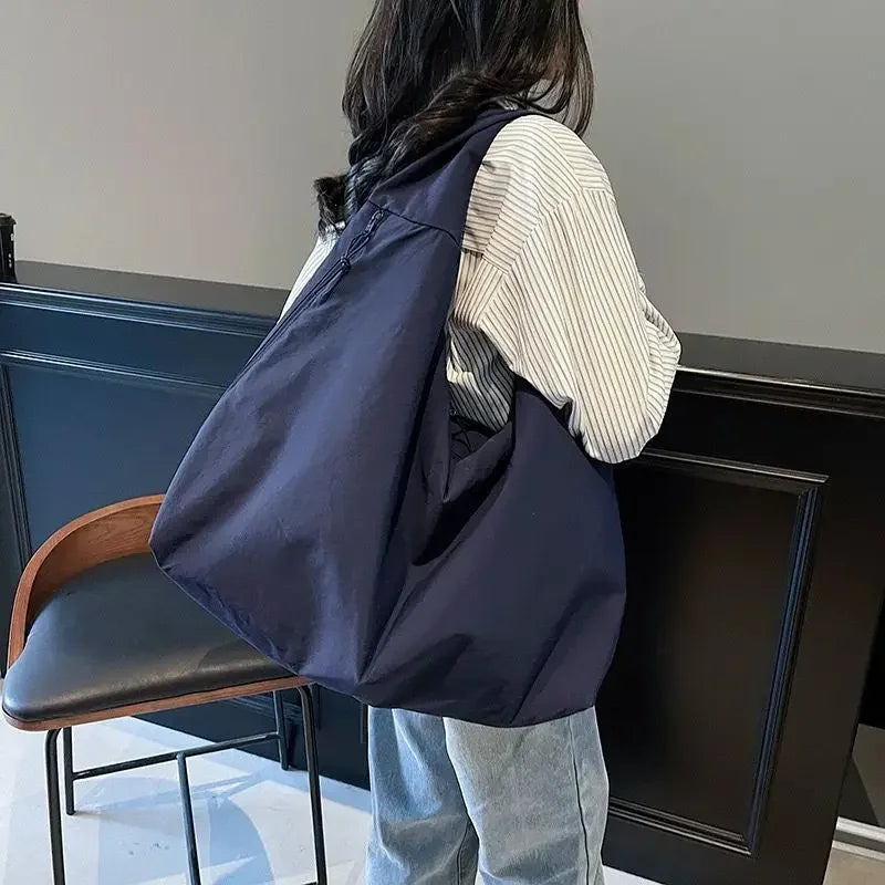 A person is standing next to a dark cabinet holding a navy blue lightweight nylon tote bag.
