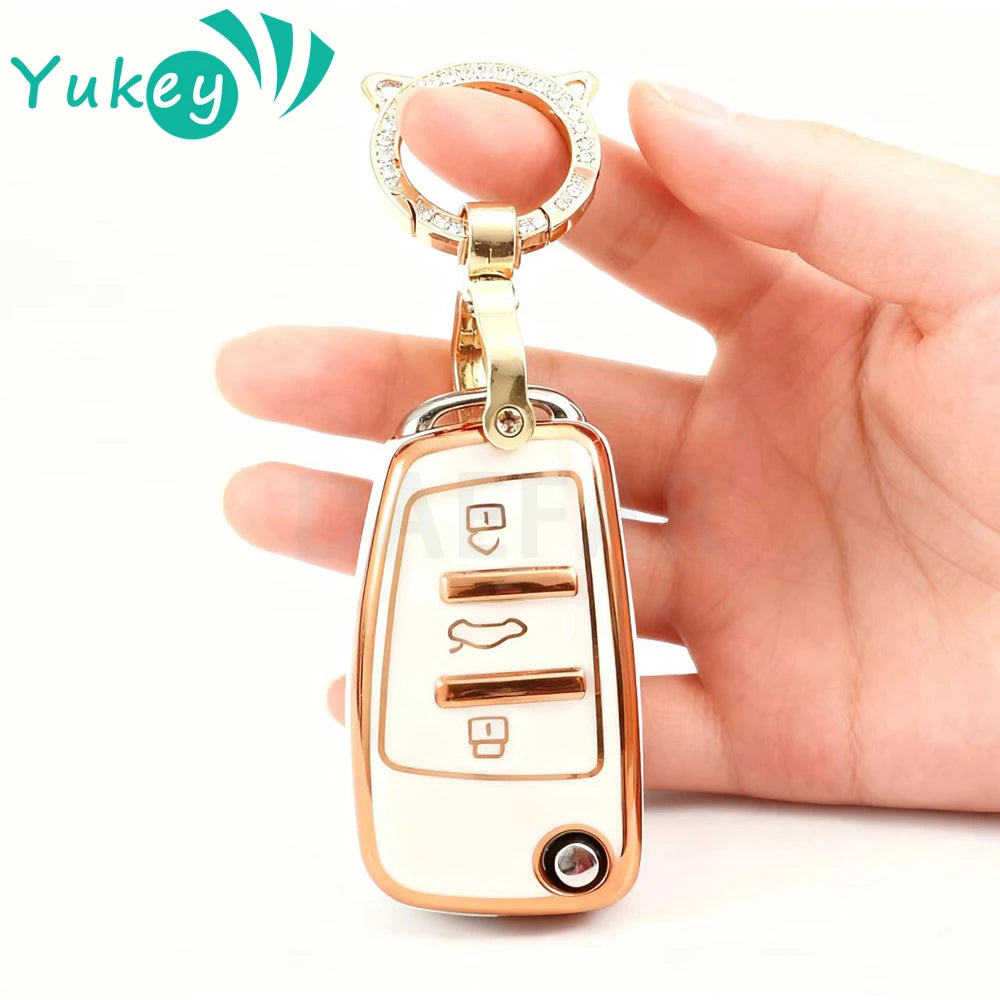 A hand holds a gold-toned protective TPU key fob cover for an Audi flip key.