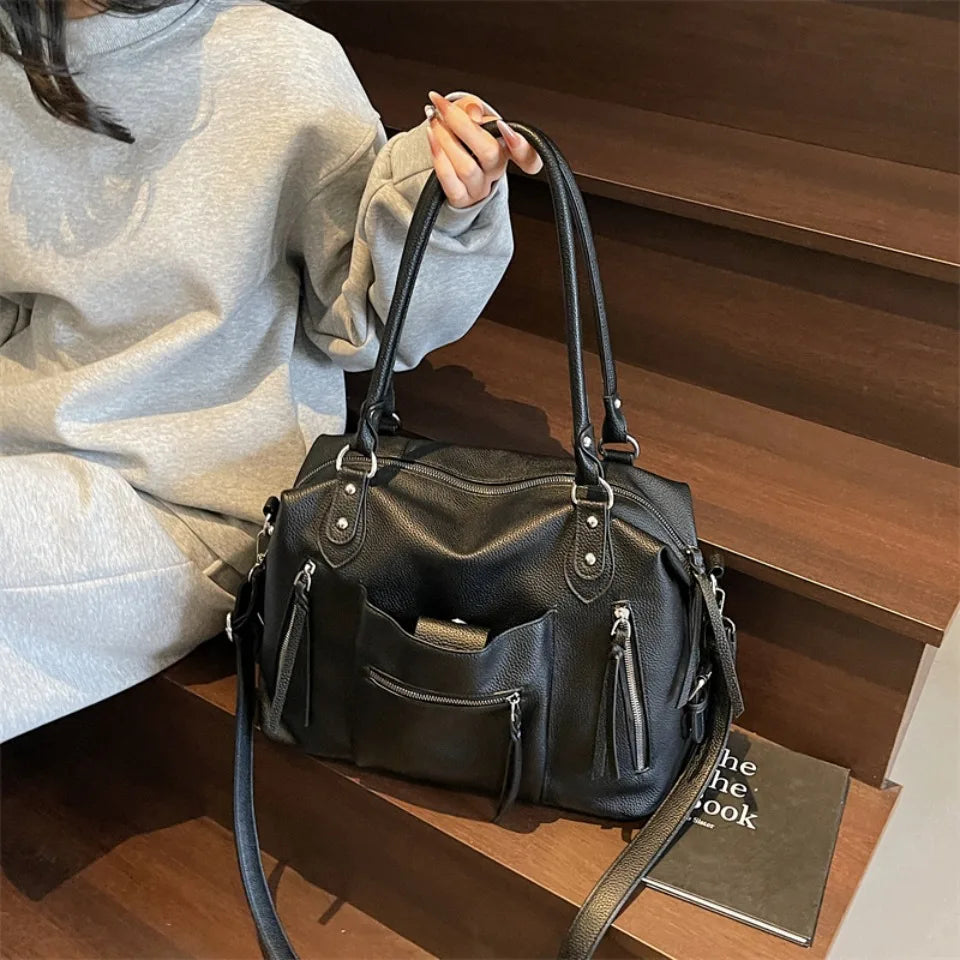 A black soft leather plaid crossbody bag with a long strap is shown resting on a wooden surface next to a person wearing a li