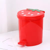 A bright red mini strawberry trash can with a green pop-up lid sitting on a white surface.