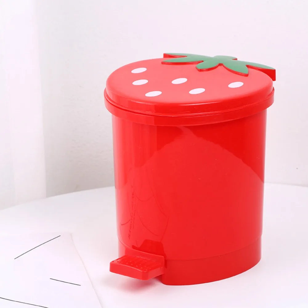 A bright red mini strawberry trash can with a green pop-up lid sitting on a white surface.