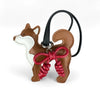 A brown faux leather dog charm shaped like a fox head with white accents and a red braided bow on a black strap.