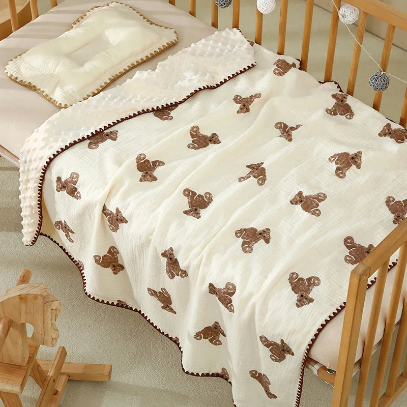 A cream cotton gauze baby swaddle blanket with a brown bear print, draped over a wooden crib.