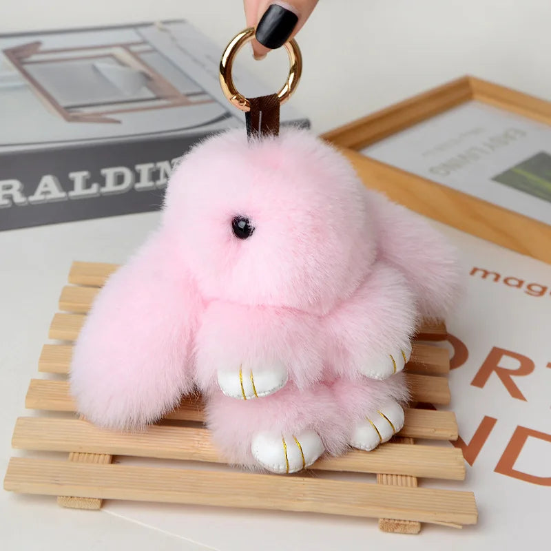 Pink fluffy angel bunny keychain with a pom pom tail resting on a wooden tray