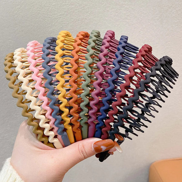Eine Hand hält einen Fächer eleganter, einfarbiger Wellen-Haarbänder in verschiedenen Rosa-, Orange-, Lila- und Blautönen.