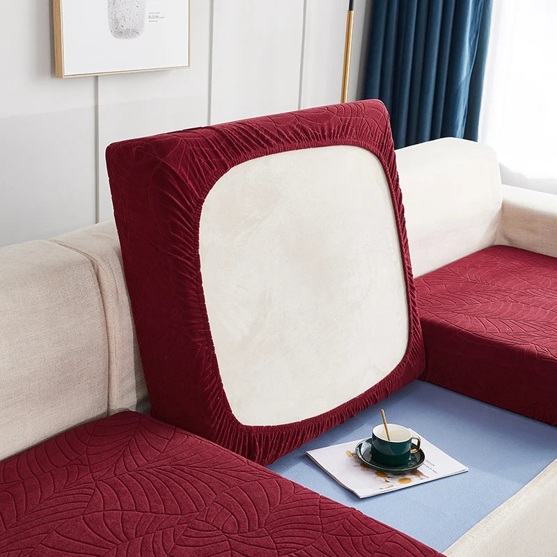 A close-up of a deep red stretch jacquard sofa cover with a light cream back and blue accents.