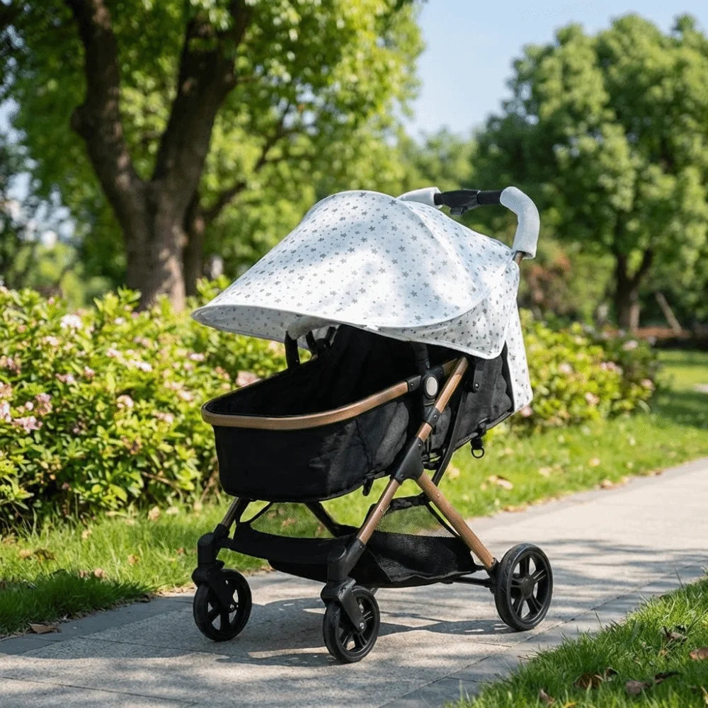A black and white stretchable UV-protective stroller sun shade is shown on a paved path with green trees in the background.