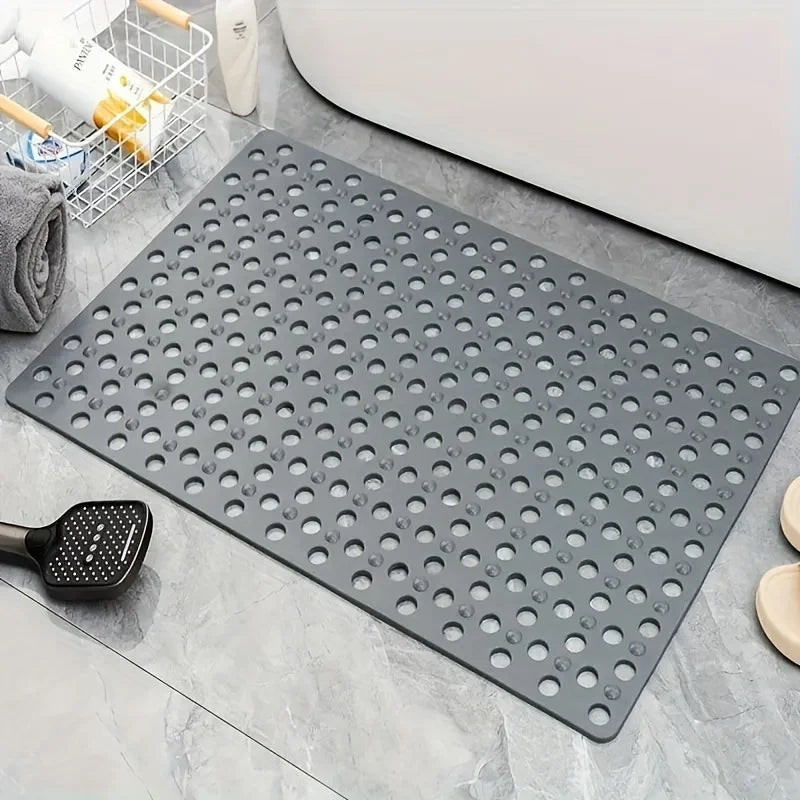 A gray anti-slip shower mat with numerous massage points and drainage holes placed on a tile surface.