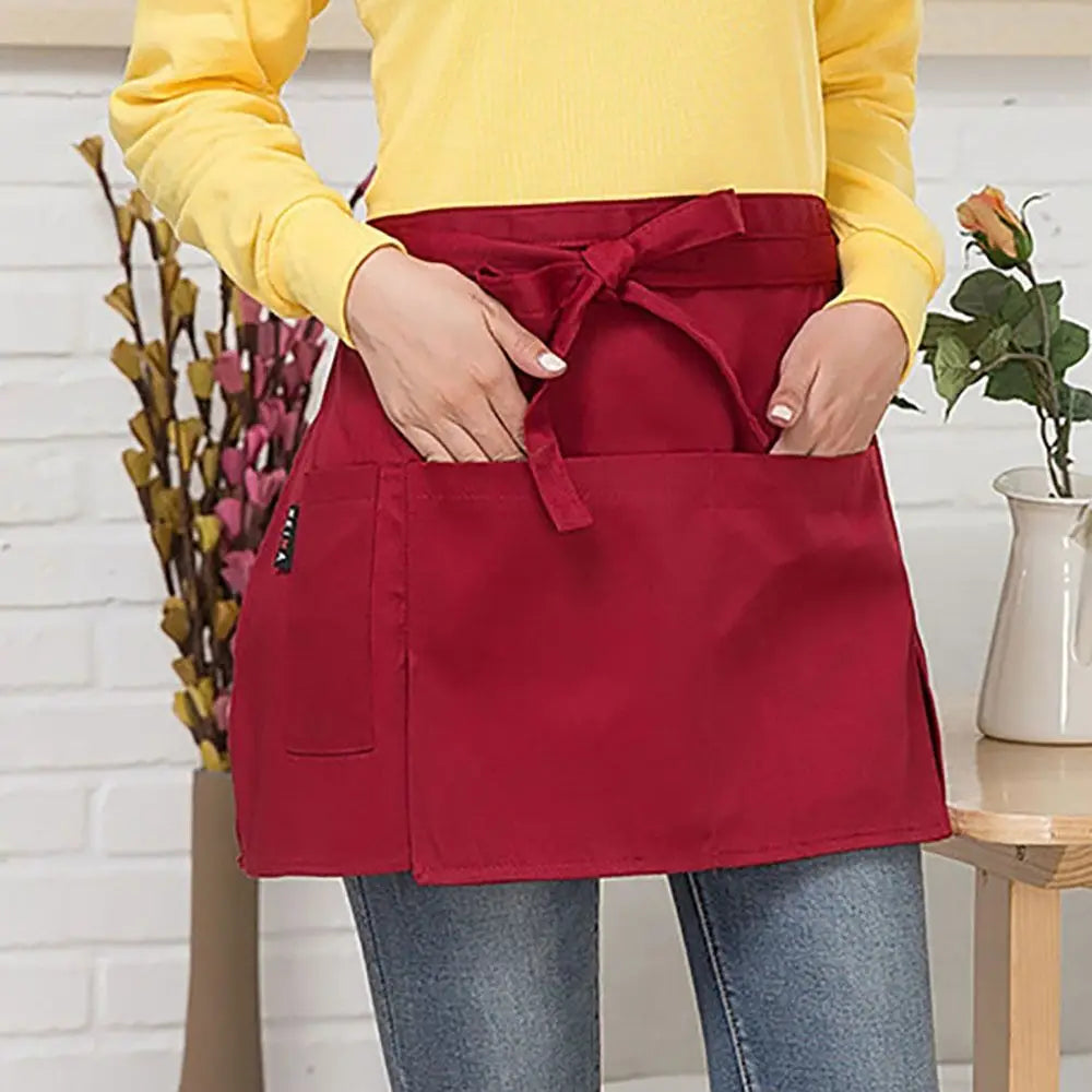 A woman wearing a red half apron with pockets over a yellow top and jeans.