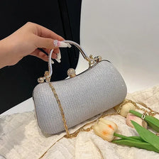 A silver shimmering envelope clutch with a gold chain strap is held by a hand on a light fabric surface.