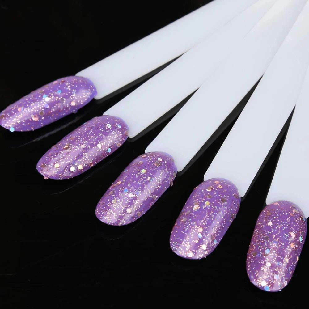 A set of clear acrylic false nail tips with purple glitter finish displayed on a black background.