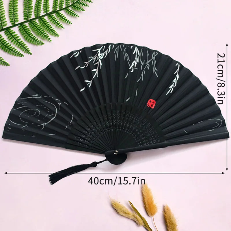 Black folding hand fan with white floral design and a durable handle displayed on a pink background.