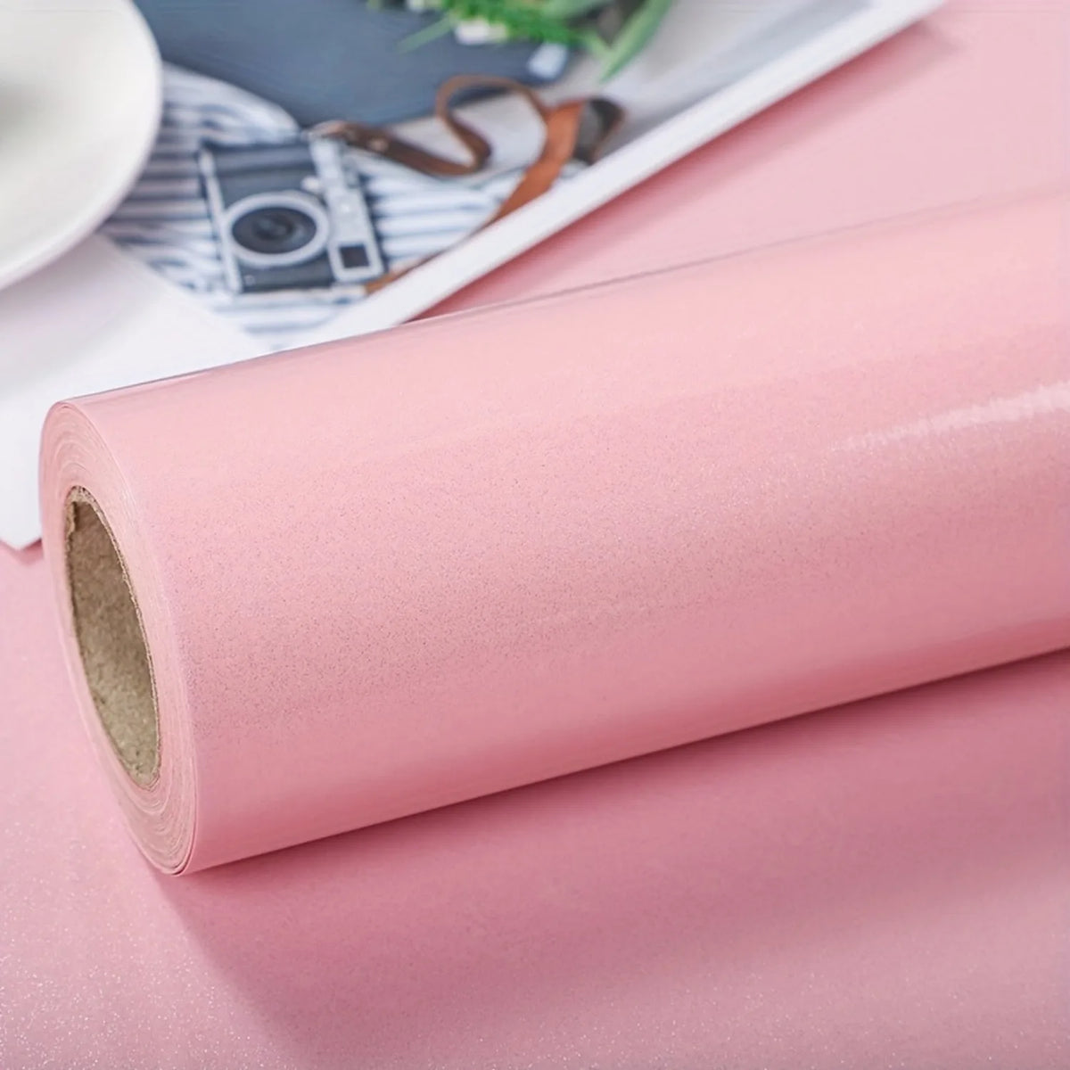 Roll of pearlescent pink marble peel and stick wallpaper lying on a pink surface.