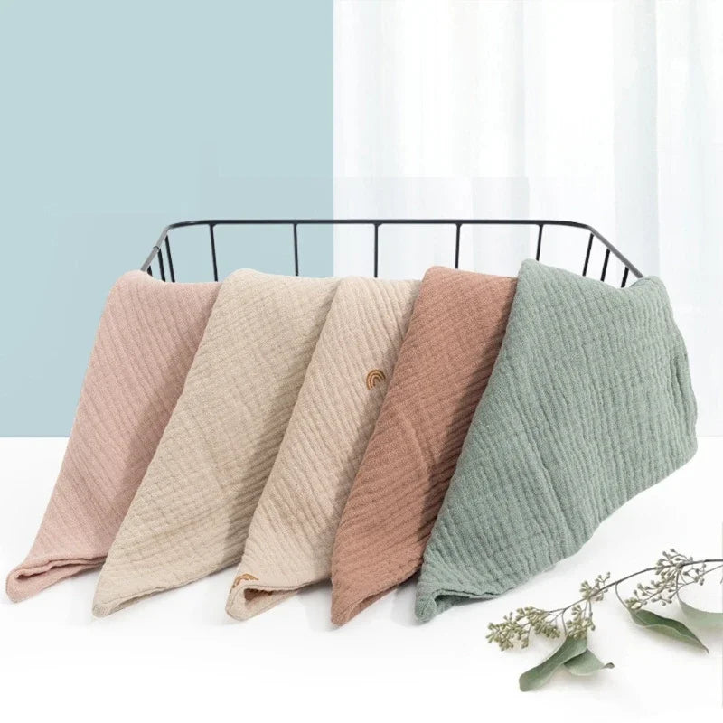 Five soft cotton gauze burp cloths in pastel shades laid out on a black wire rack.