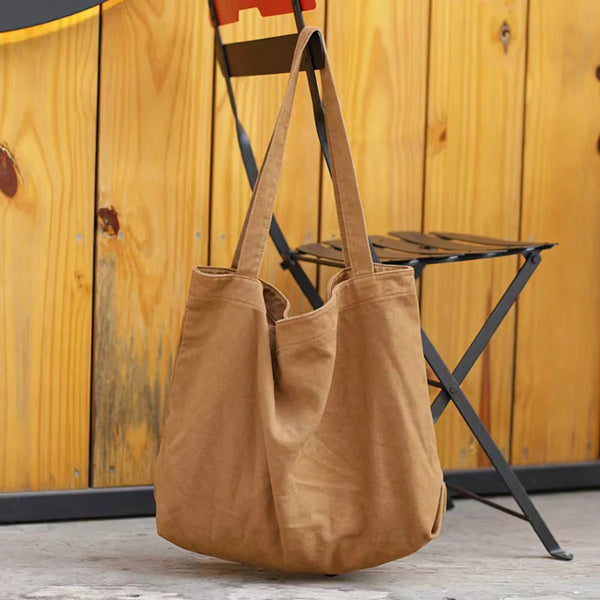 Sac cabas en toile marron accroché sur un fond en bois à côté d'un tabouret pliable noir.