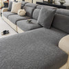 A gray jacquard fleece sofa cover with a textured pattern and anti-slip backing shown on a sectional sofa.