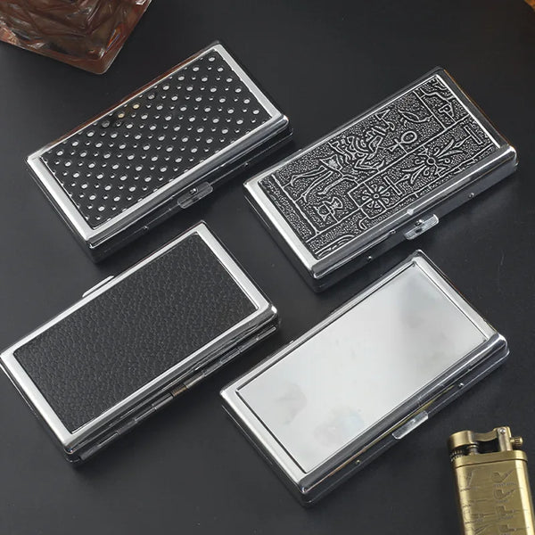 Three slim metal cigarette cases with different textures and engravings are displayed on a dark surface.
