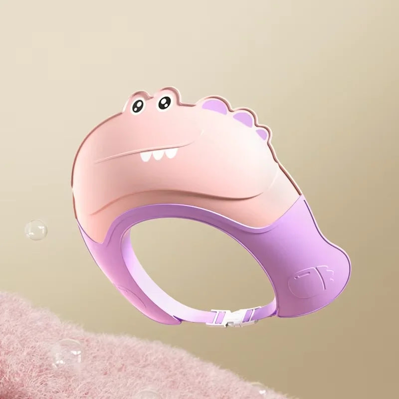 A pink and purple adjustable baby bath shampoo shield cap with ear protection is shown against a soft pink background.