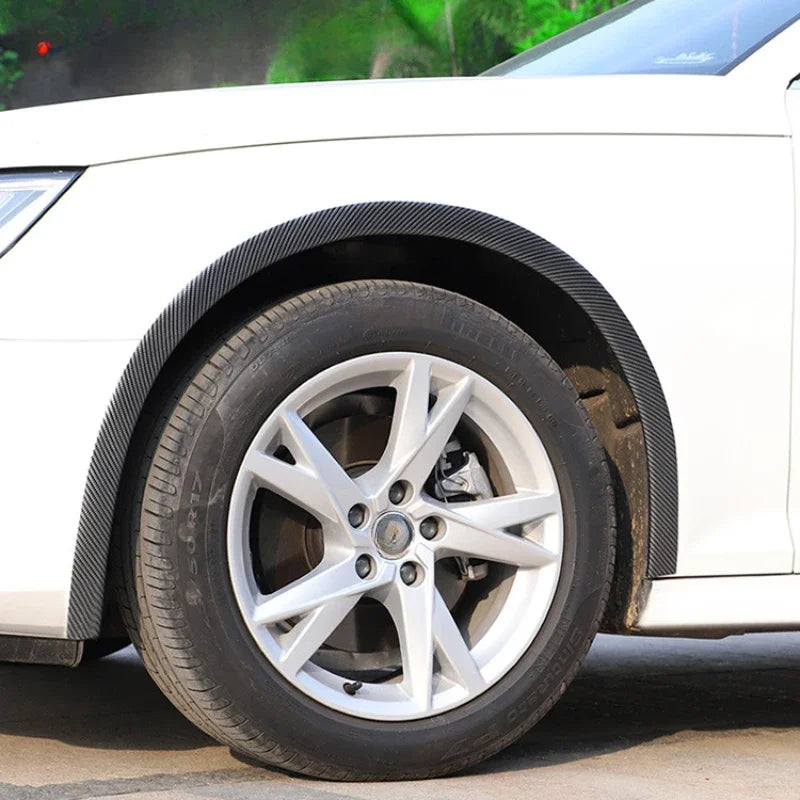 Close-up of a white car showing carbon fiber wheel arch trim strips and alloy wheels.