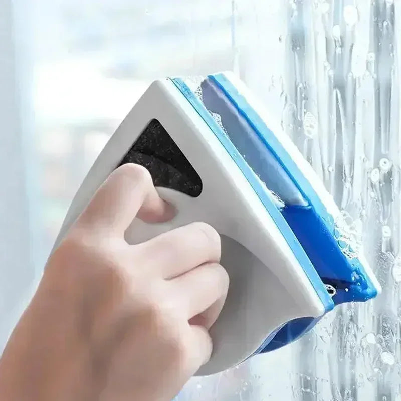 A hand is using a white magnetic double-sided window cleaner with a blue safety rope to clean a window.
