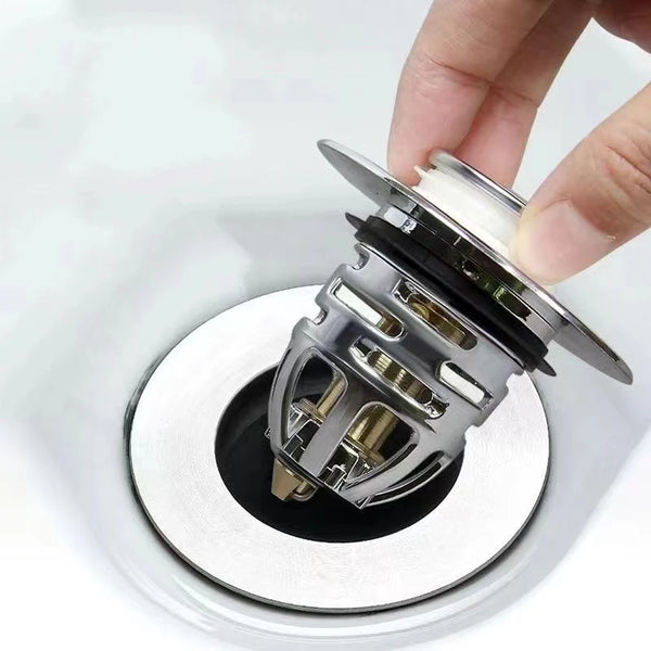 A hand is holding a silver pop-up sink drain stopper, showing the mechanism for use.